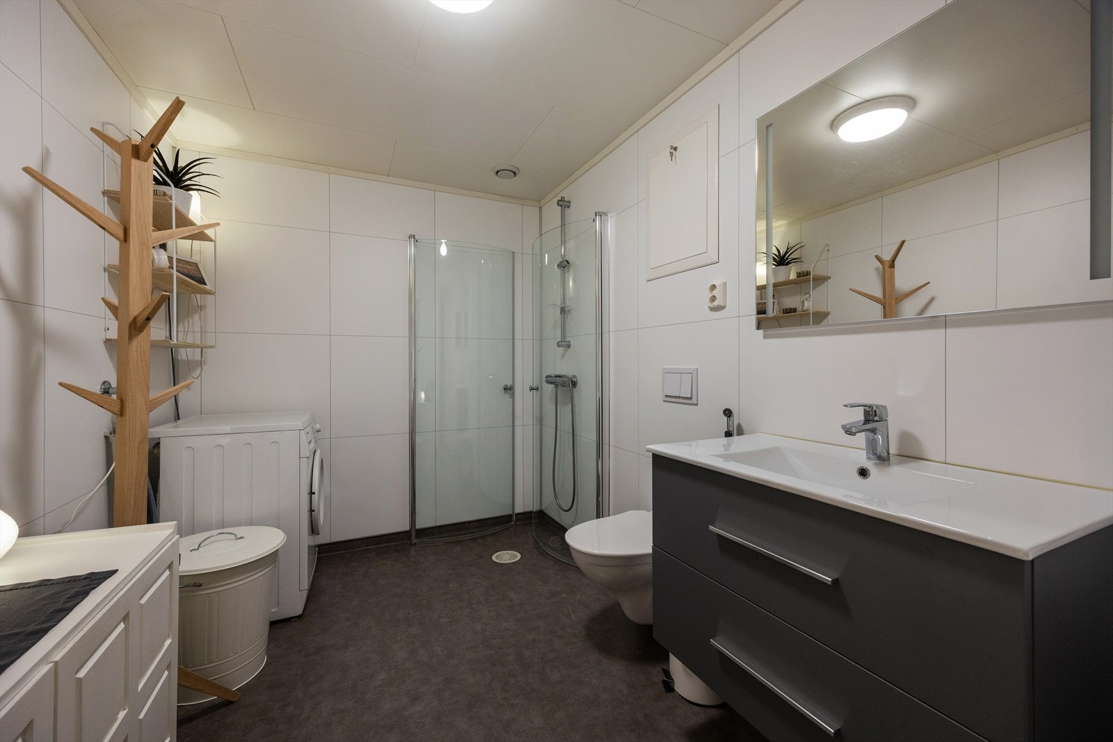 Rommet er innredet med en servant nedfelt i baderomsinnredningen, et veggmontert toalett og et dusjhjørne med dusjvegger. Det er også praktisk opplegg for vaskemaskin. Galleribilde