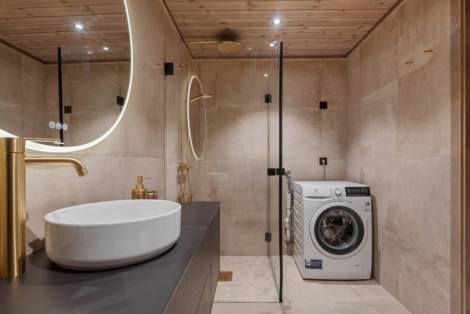 Begge bad har flislagte overflater på både vegger og gulv, med elektriske varmekabler i gulvet for komfort. Himlingen er kledd med beiset panel og har innfelte spotter som gir god belysning. Galleribilde