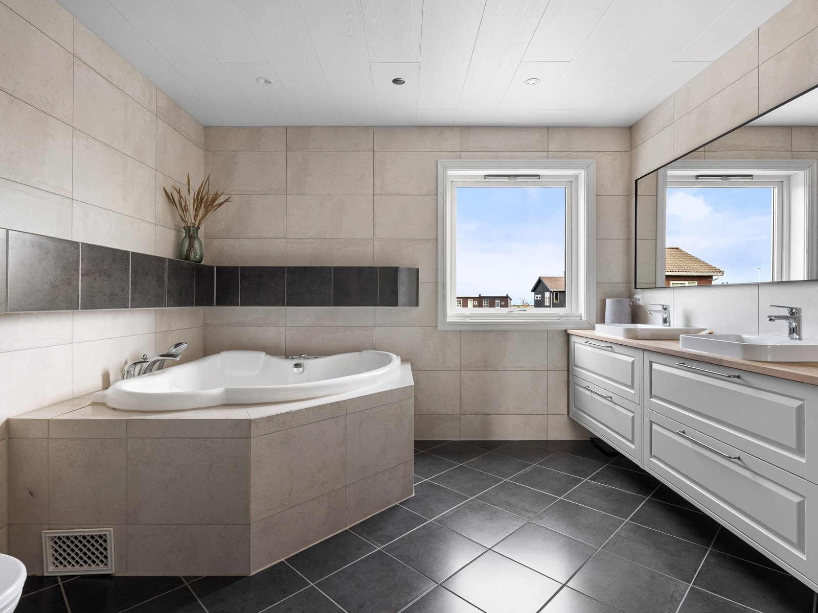 Familiebadet er flislagt og innholdsrikt, med dobbel servant, hjørnebadekar, dusj og veggmontert toalett. Galleribilde