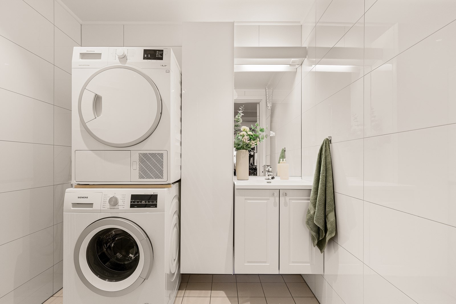 Bad/vaskerom m/dusjhjørne m/glassvegger, servantskap, speil, høyskap og opplegg til vaskemaskin Galleribilde