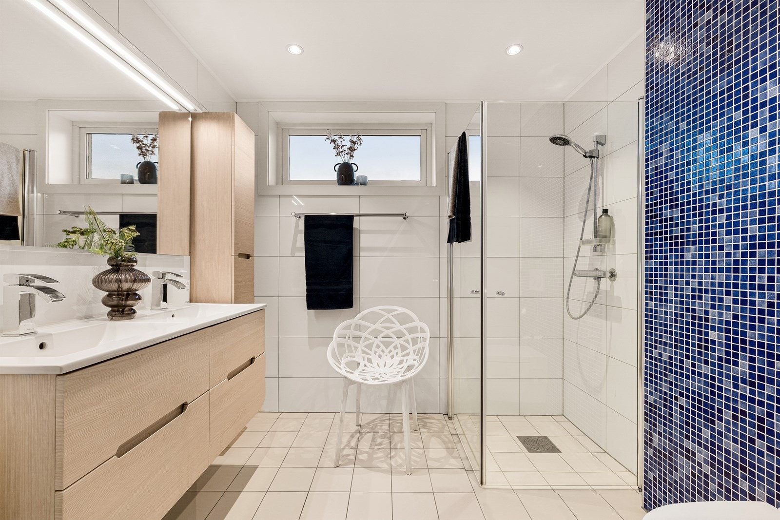 Delikat bad- dusjhjørne med glassvegger, innredning med dobbel servant, speil, to høyskap og elektrisk vegghengt toalett med vannspyling Galleribilde