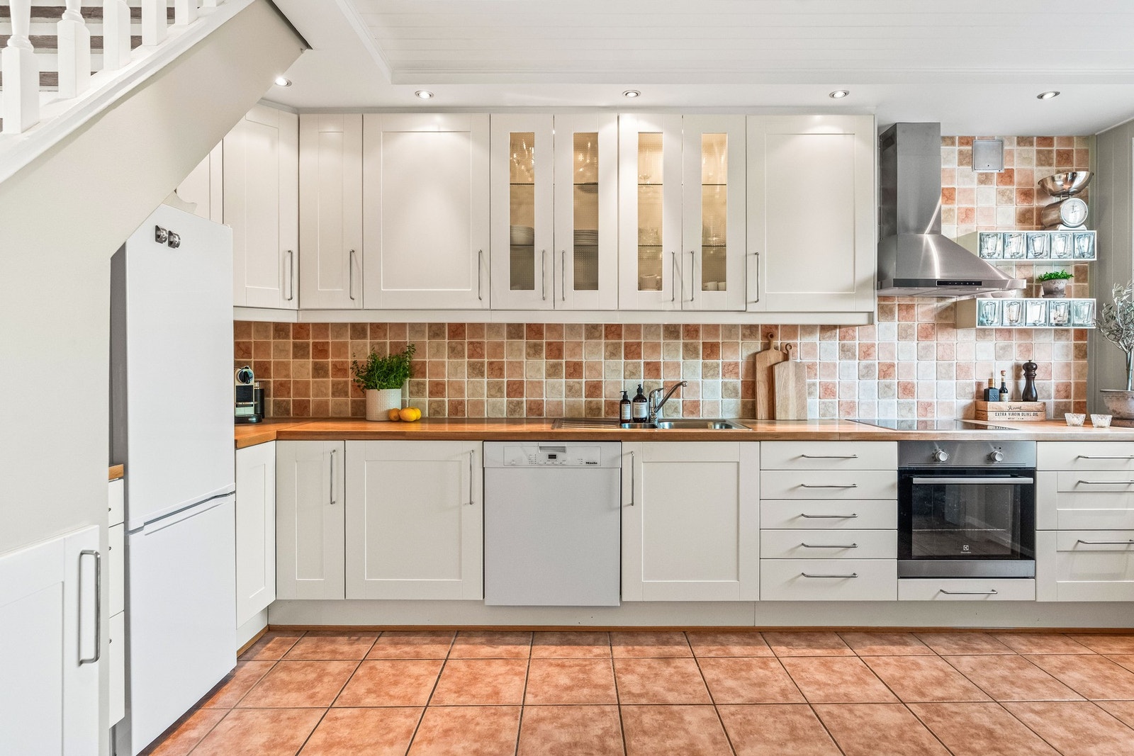 Funksjonelt kjøkken med profilerte, slette og vitrine fronter. Flislagt over benk og på gulvet som gjør det lett å rengjøre. Galleribilde