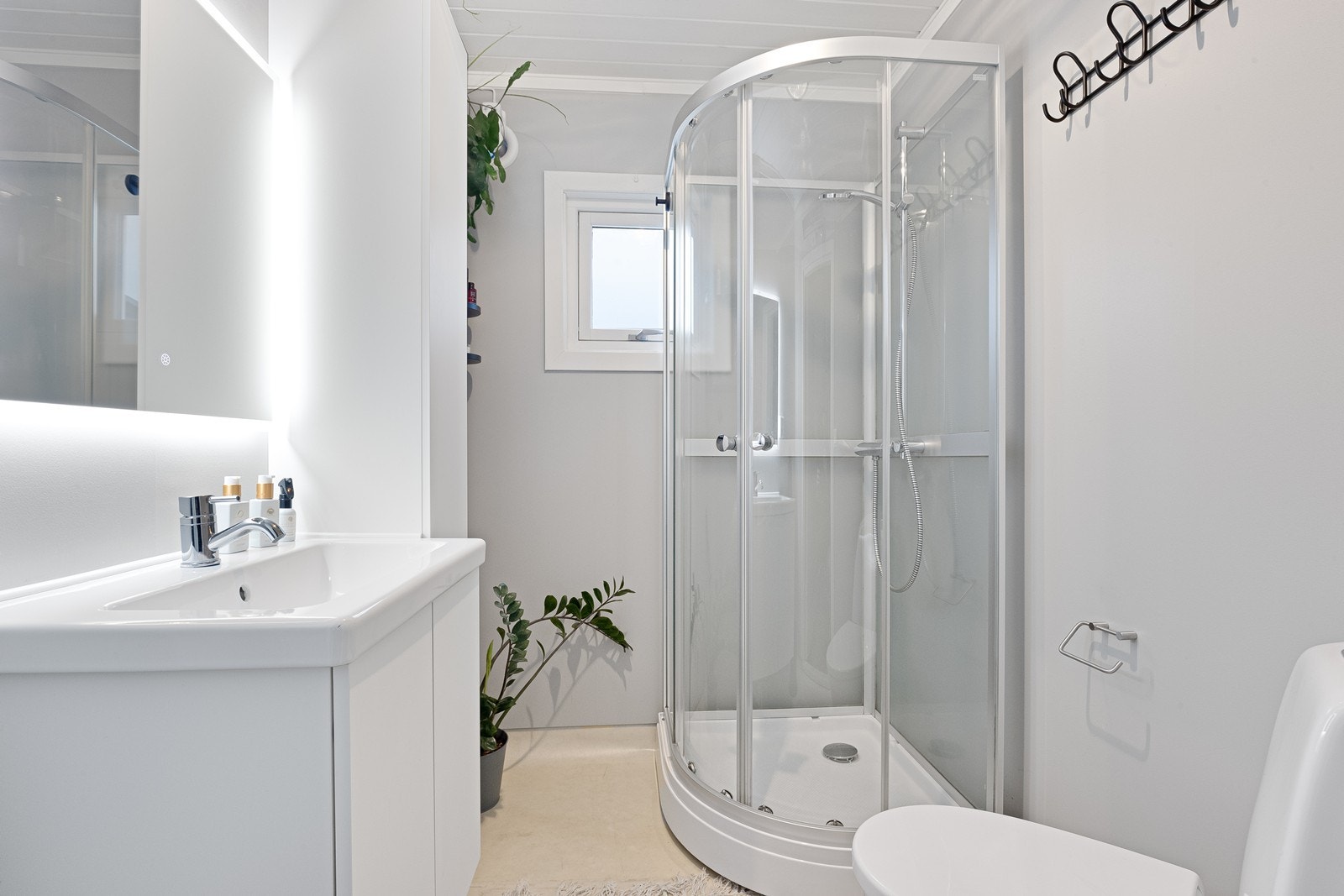 Nyere dusjkabinett og gulvstående toalett gir praktisk våtromsløsning. Elektrisk styrt vifte i vegg sikrer ventilasjon. Galleribilde