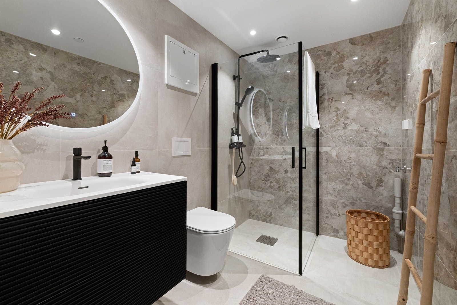Eksklusivt bad med store fliser i elegante naturtoner. Servantskap i mørk utførelse med ovalt LED-speil, integrert lys og gulvvarme. Galleribilde