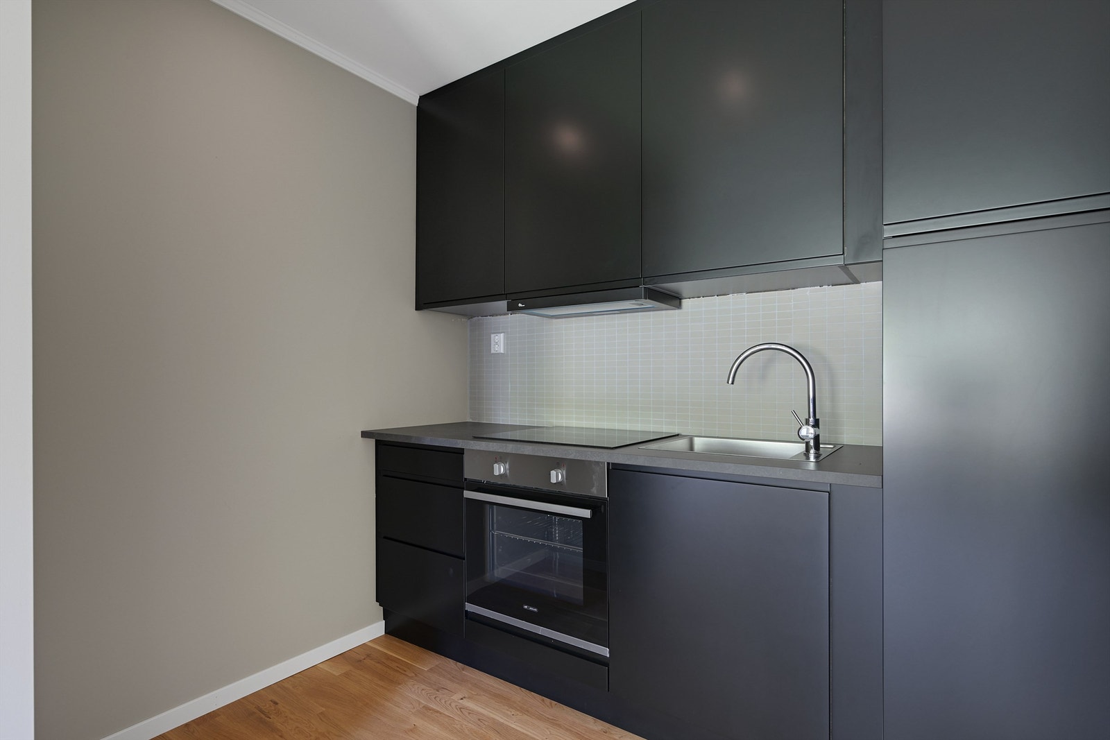 Kjøkkenet har mørke glatte fronter med benkeplate av laminat. Galleribilde