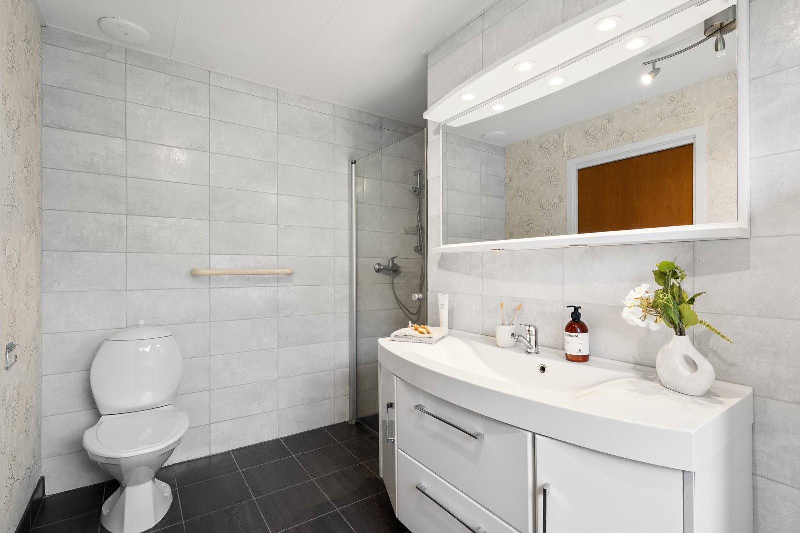 Gulvet har mørke fliser, i kombinasjon med mønstret tapet og lysegrå fliser på veggene. Galleribilde