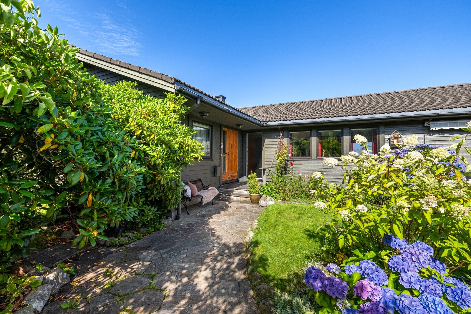 På fremsiden har tomten en asfaltert gårdsplass, og herfra er det en steinlagt gangsti opp til hovedinngangen. Galleribilde