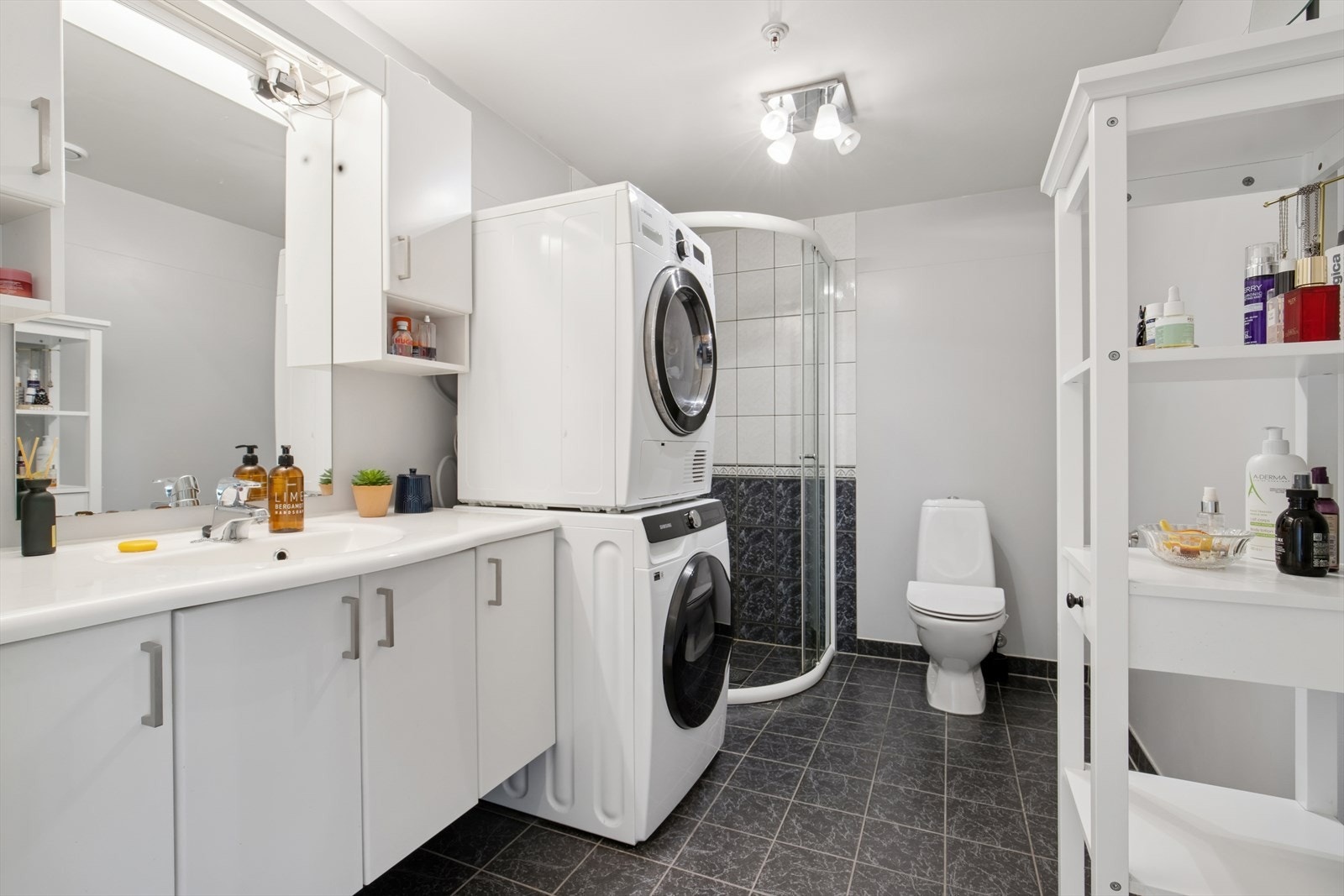 Baderom av god størrelse med plass til både vaskemaskin og tørketrommel. Bred servant med belysning over speil og i tak. Galleribilde