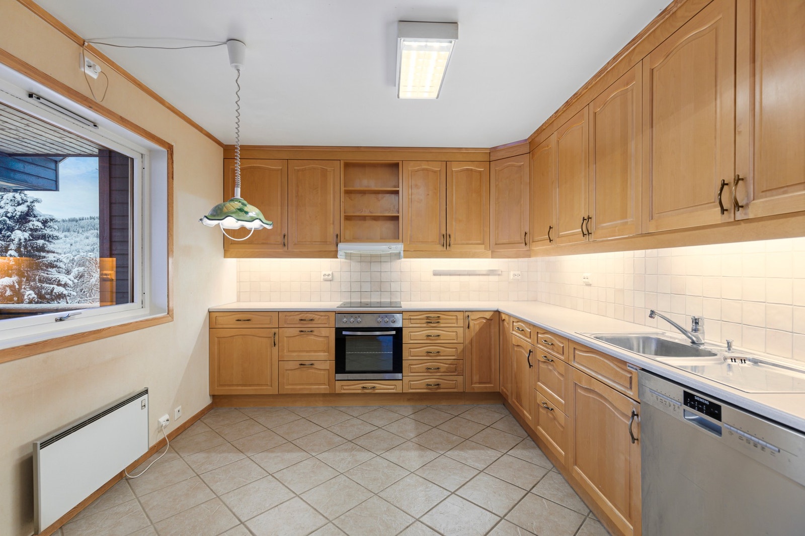 Kjøkken fra 2001 med L-formet innredning fra Espe Trevarefabrikk bestående av benkeskap og takhøye overskap med profilerte fronter av sibirsk lerk Galleribilde