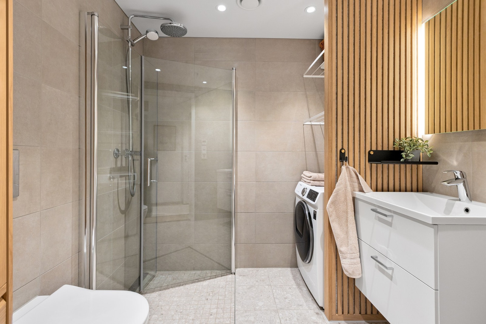 Badet er moderne og delikat med flislagte overflater. Dusj med innfellbare glassdører i herdet glass. Galleribilde