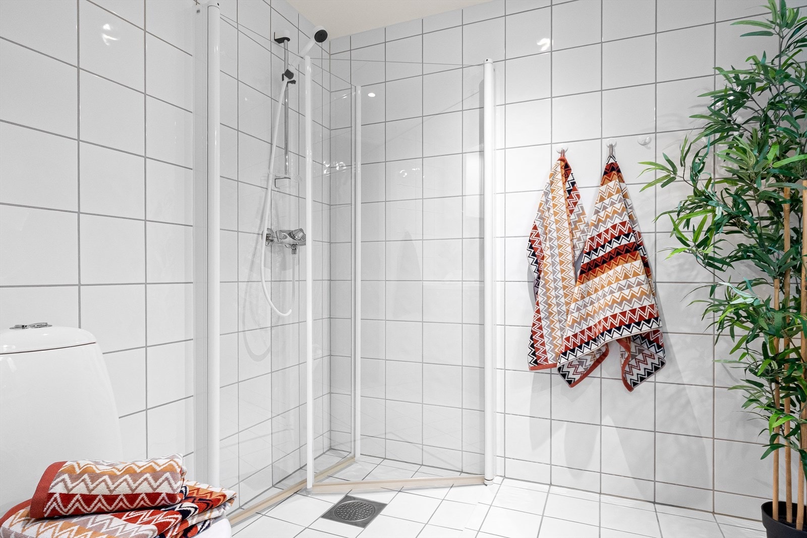 Badet er innredet med et servantskap med servant, et gulvmontert toalett og en vegghengt dusj med skjermdører i glass. Galleribilde