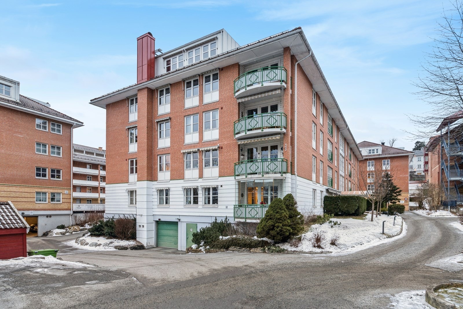 Garasjeinngang med portåpner. Gjesteparkering på begge sider fra innkjørselen. Inngang til høyre for blokken. Galleribilde