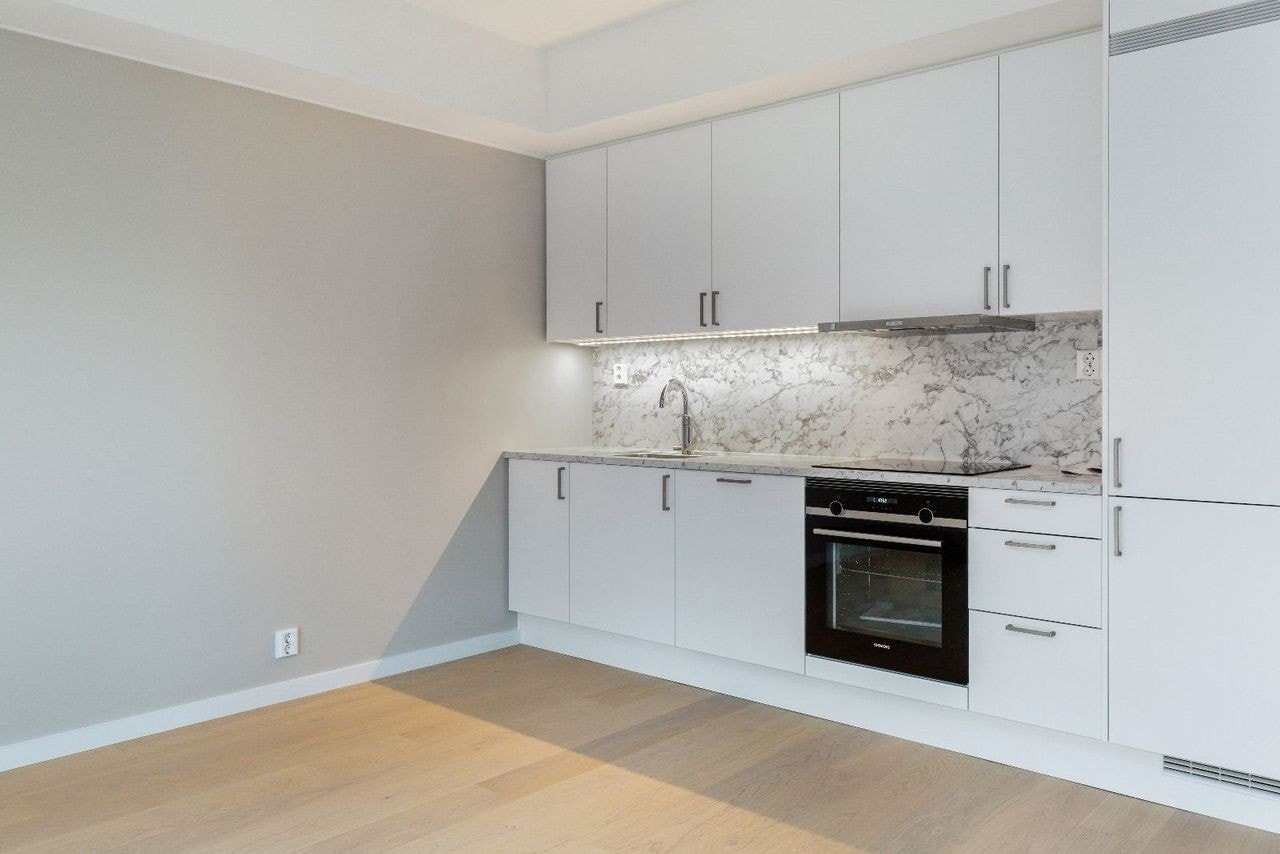 Stilrent kjøkken med integrerte hvitevarer og åpen løsning mot stue. Galleribilde