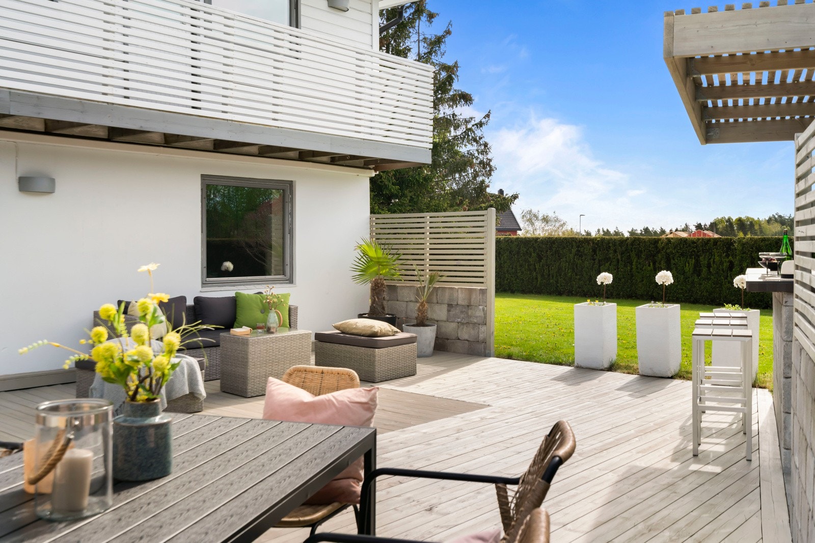 En vakker, tett hekk rammer inn tomten på tre sider og skjermer de solrike uteplassene, som er parkmessig opparbeidet med terrasseplatting i tre, dekorativ belegningsstein og en oppmurt bar- og grillløsning under tak. Galleribilde