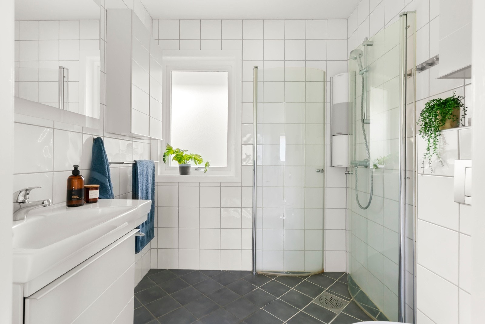 Innbydende bad fra 2007 med fliser og varmekabler under. Badet er utstyrt med vegghengt toalett, nyere hvitprofilert baderomsinnrednings kombinert med speilskap og to veggskap. Dusjhjørne med innfellbare glassvegger. Galleribilde