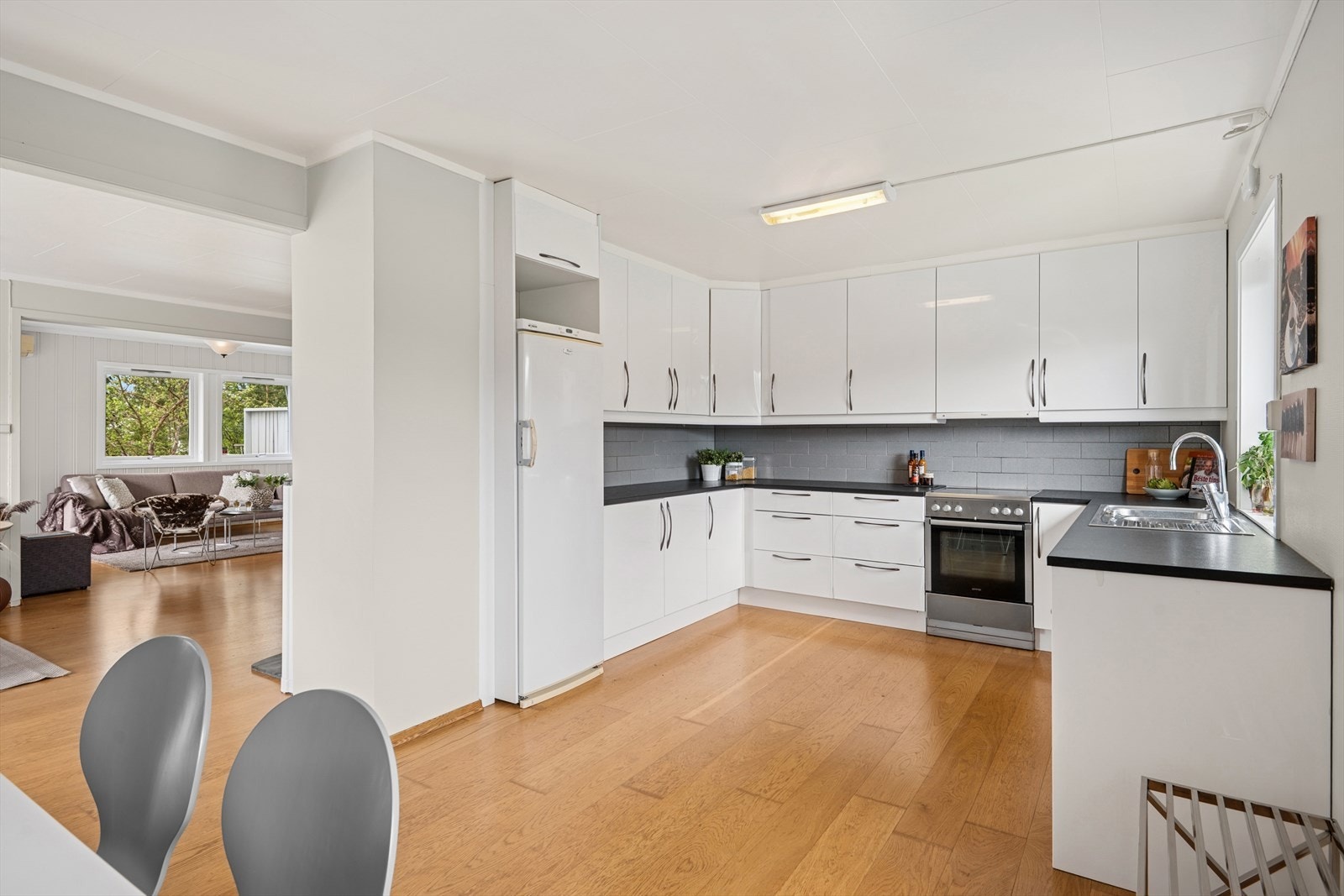 Kjøkkeninnredningen er takoppforet og har hvite, glatte fronter med benkeplate i laminat. Det er fliser på vegg mellom benkeplate og overskap. Galleribilde