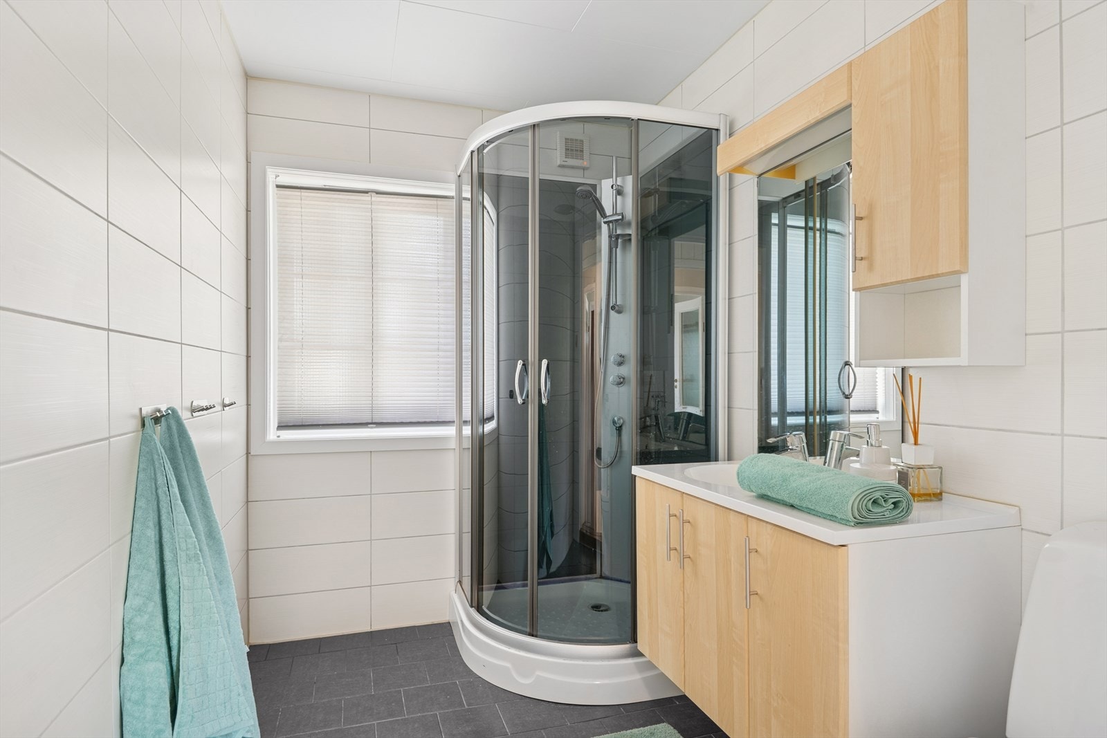 Badet er stilrent med fliser på gulv og vegger. Det er utstyrt med dusj, toalett og servant med oppbevaringsplass og speil. Galleribilde