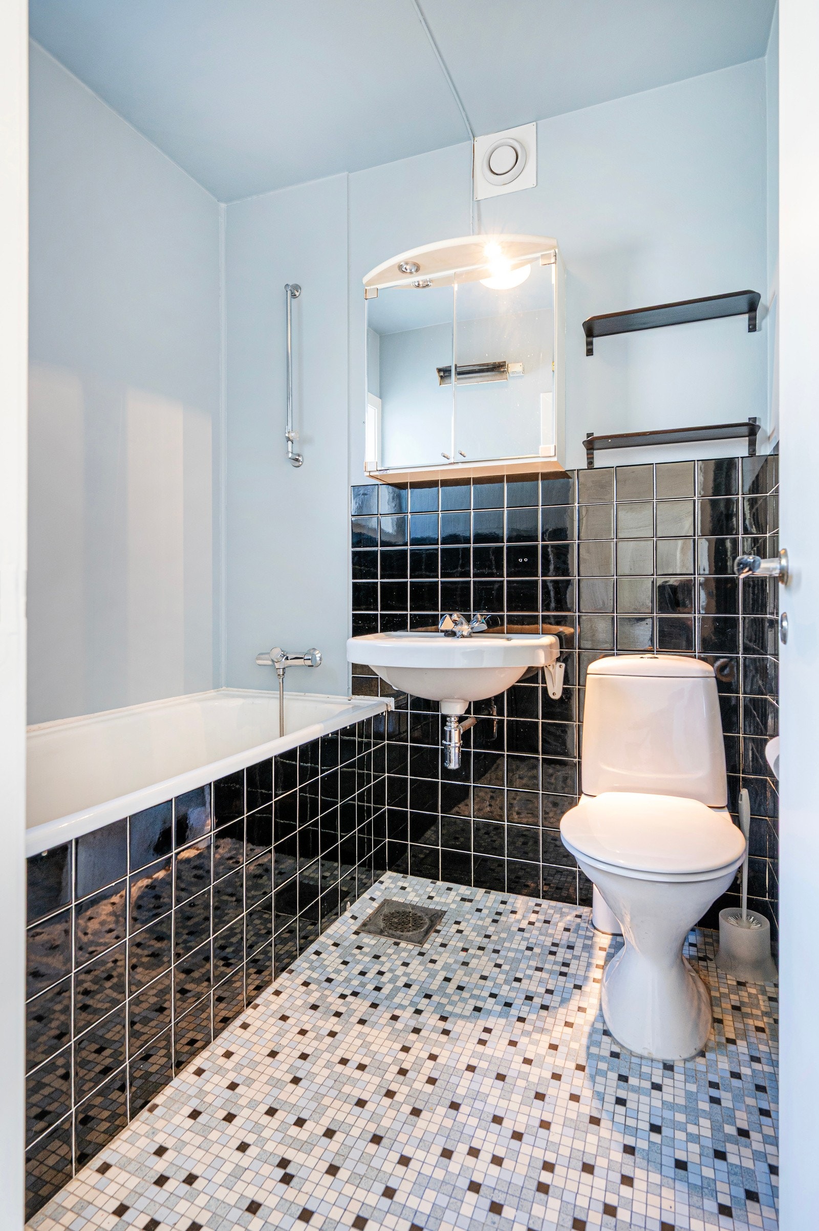 Bad med fliser på gulv og til brystning på vegg. Her er badekar, servant og toalett. Galleribilde