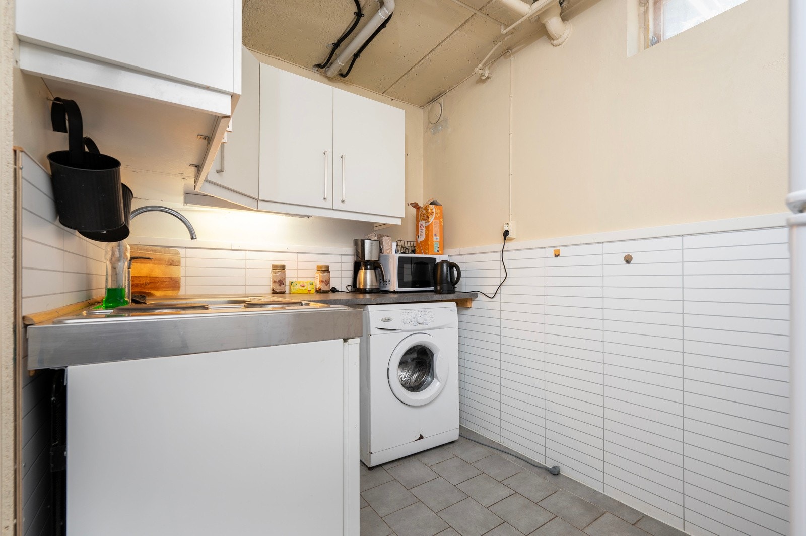 Hybelkjøkken med enkel innredning og med opplegg for vaskemaskin. Galleribilde