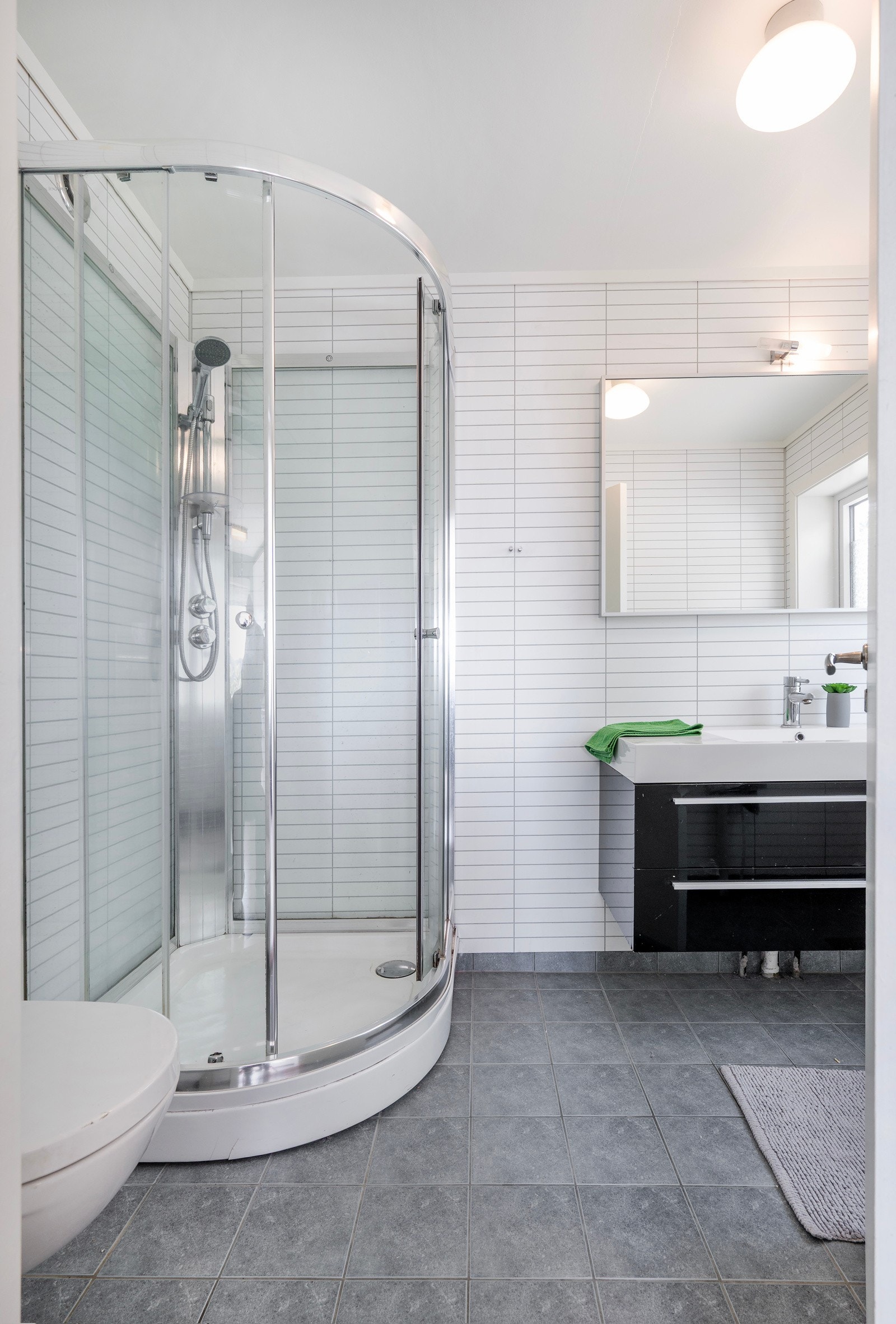 Bad med fliser på gulv og våtromsplater på veggene. Her er dusjkabinett, vegghengt toalett og innredning med servant. Galleribilde