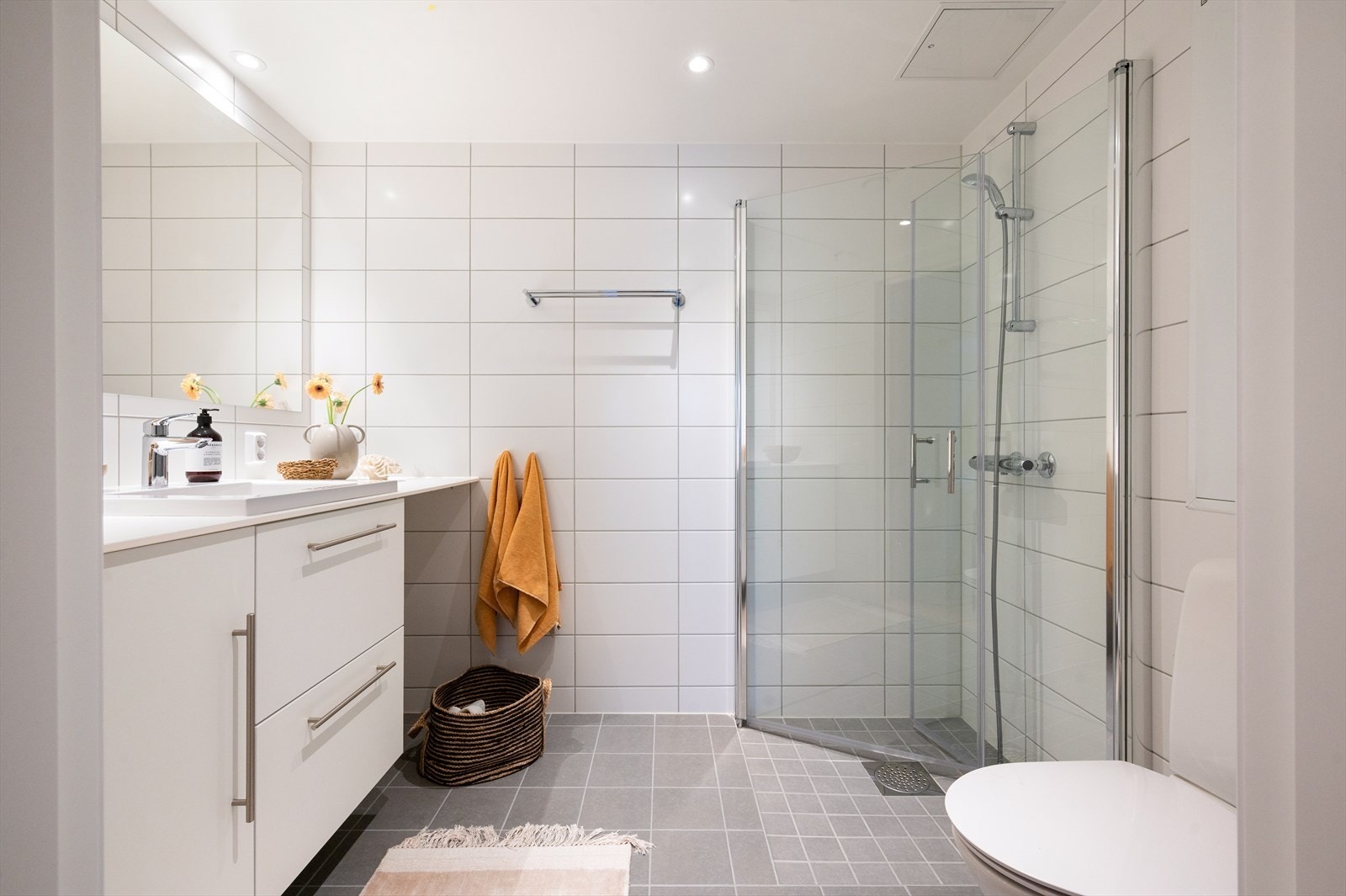 Romslig baderom med dusjhjørne og innfellbare dusjvegger, vegghengt toalett og opplegg for vaskemaskin under praktisk benkeløsning. Galleribilde