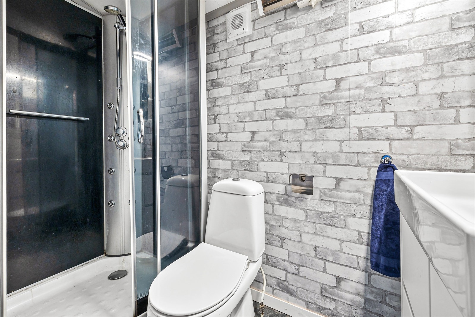 Bad med servant over servantskap, gulvstående toalett og dusjkabinett med massasjedyser Galleribilde