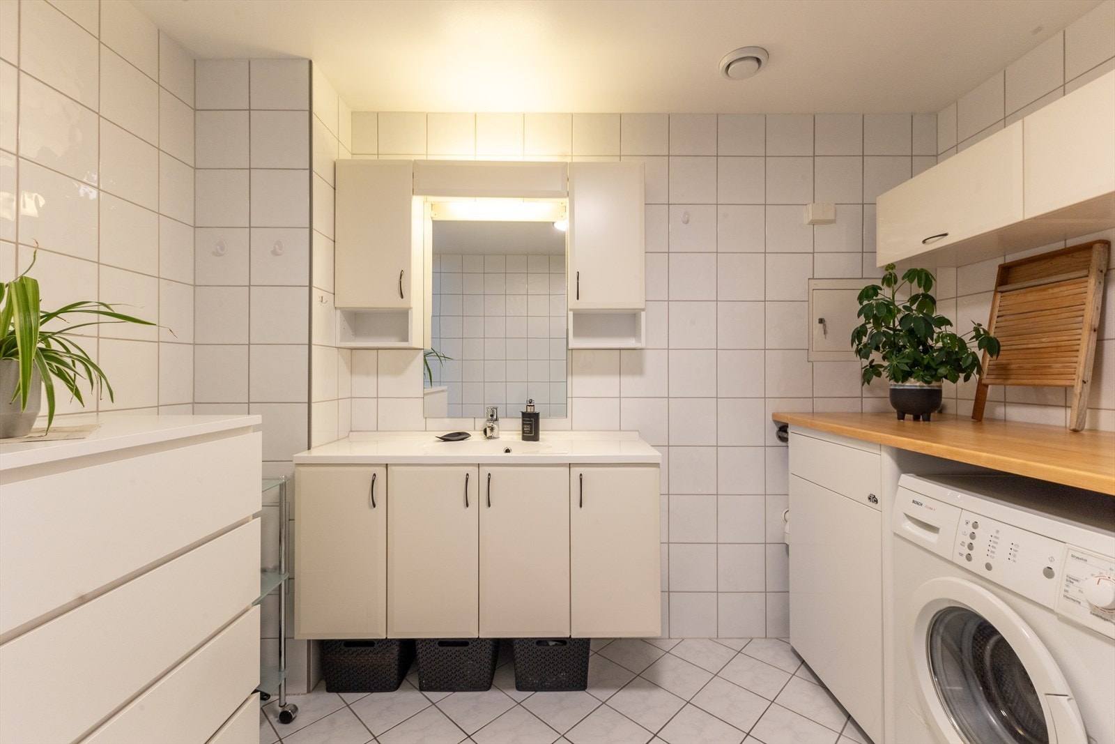 Romslig baderomsinnredning og praktisk løsning med benkeplate over bla. vaskemaskin, for å kunne brette klær etter klesvasken. Galleribilde