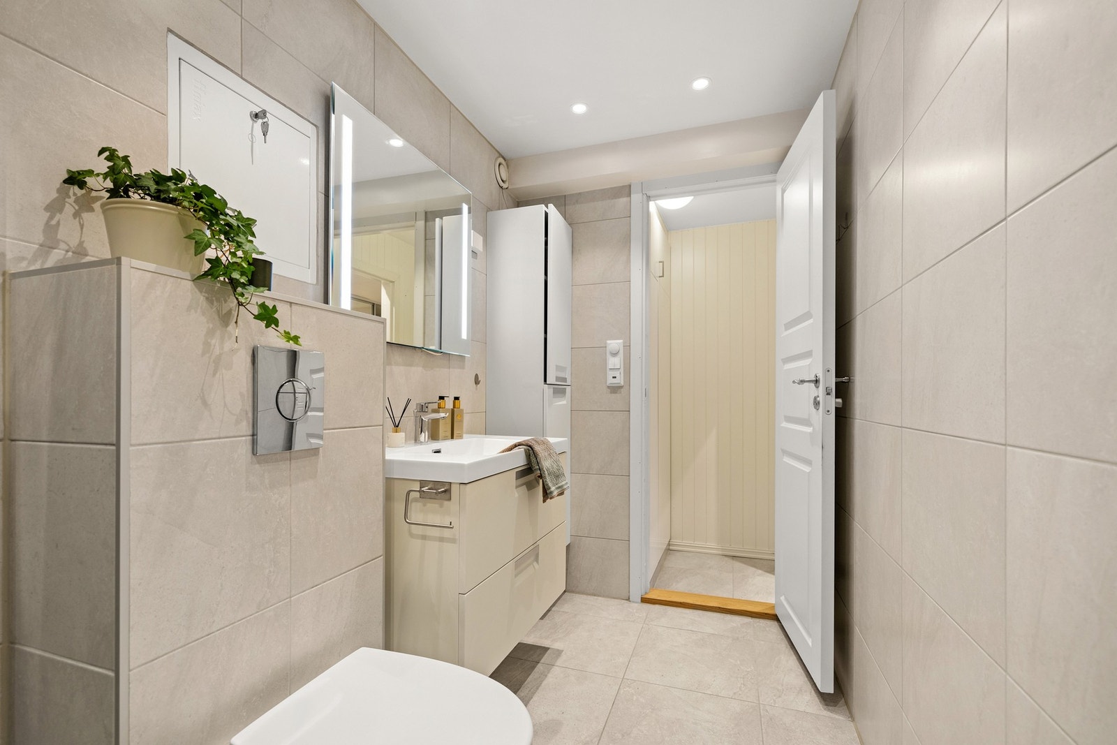 Badet har pen innredning med toalett, servant med skuffeseksjon og høyskap. Vaskemaskin i gangen utenfor Galleribilde