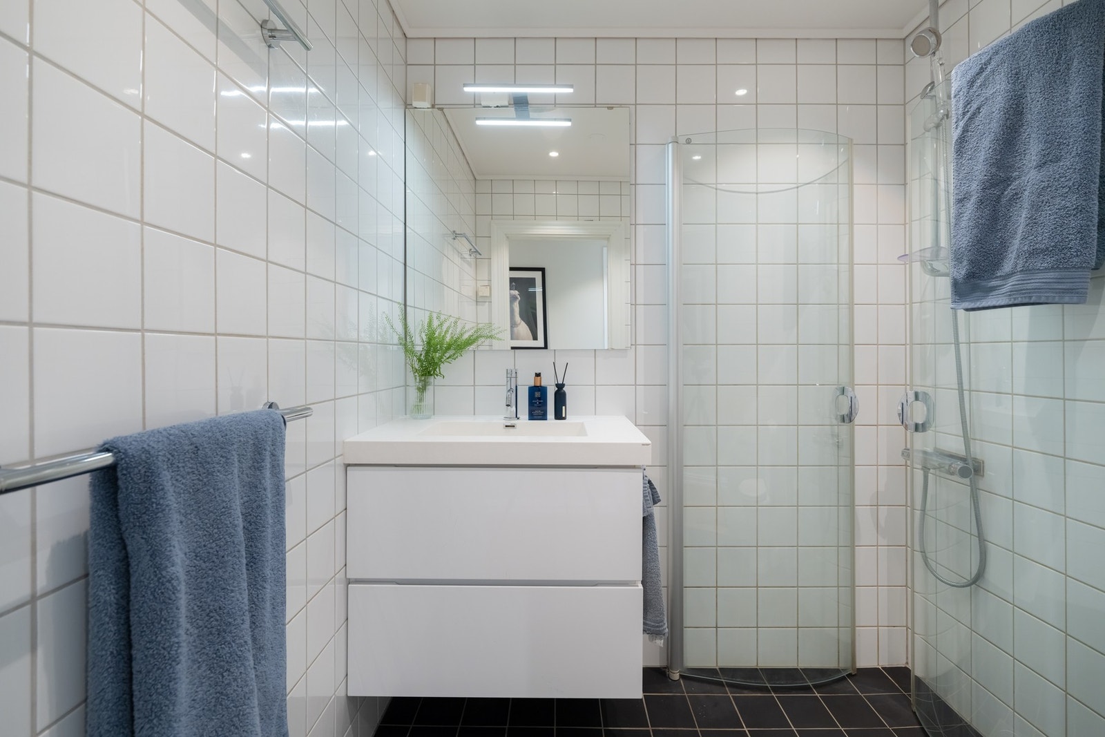 Servant med underskuffer, speil, toalett og dusjhjørne med svingbare dører som frigjør plass på gulvet. Galleribilde