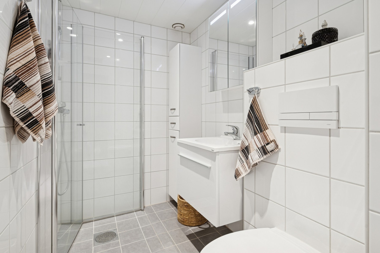 Delikat flislagt bad med dusjhjørne og innredning med god oppbevaringsplass. Galleribilde