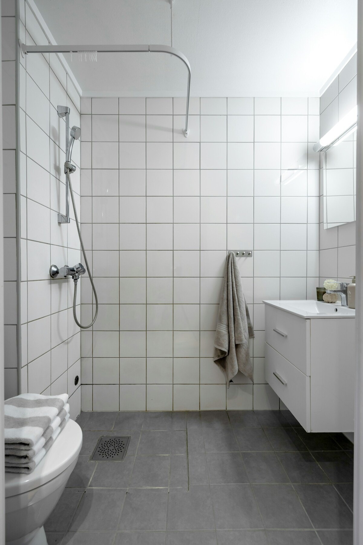 Leiligheten har et flislagt bad med dusjhjørne, toalett, servantinnredningen med to skuffefronter og speil med lys Galleribilde