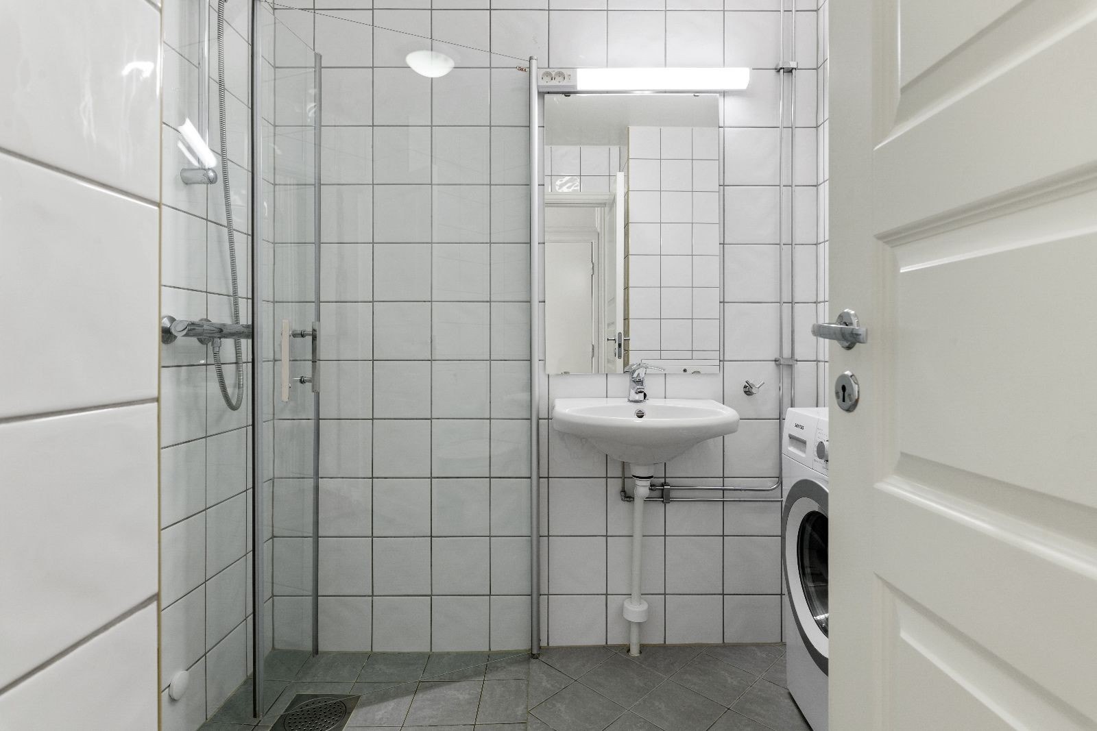 Flislagt baderom med gulvvarme, dusj, servant, toalett og vaskemaskin Galleribilde