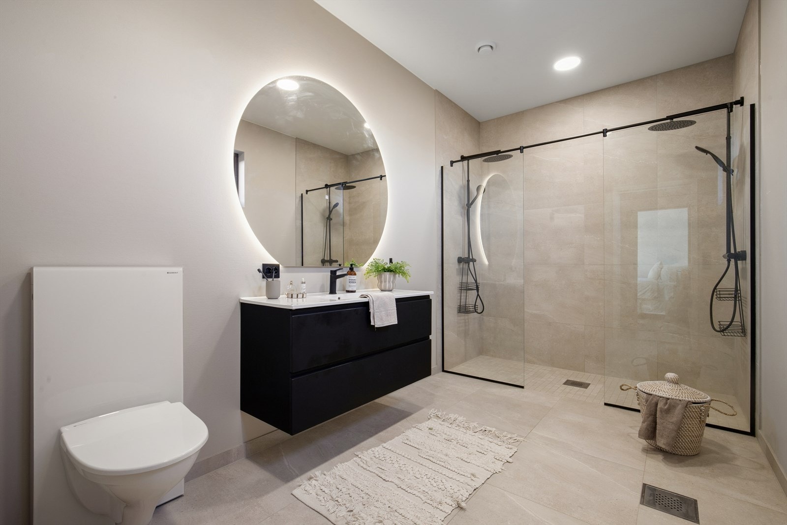 Badet er innredet med en nedfelt servant, veggmontert toalett og en dusjnisje med to dusjer og glassvegger. Galleribilde