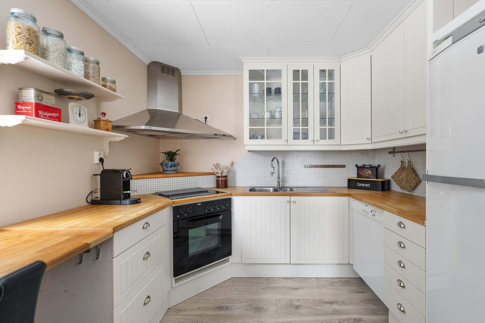 Pent klassisk kjøkken fra byggeår med profilerte kremhvite fronter og vitrineskap, foring opp til tak. Benkeplate i heltre med nedfelt vaskekum i rustfritt stål. Galleribilde