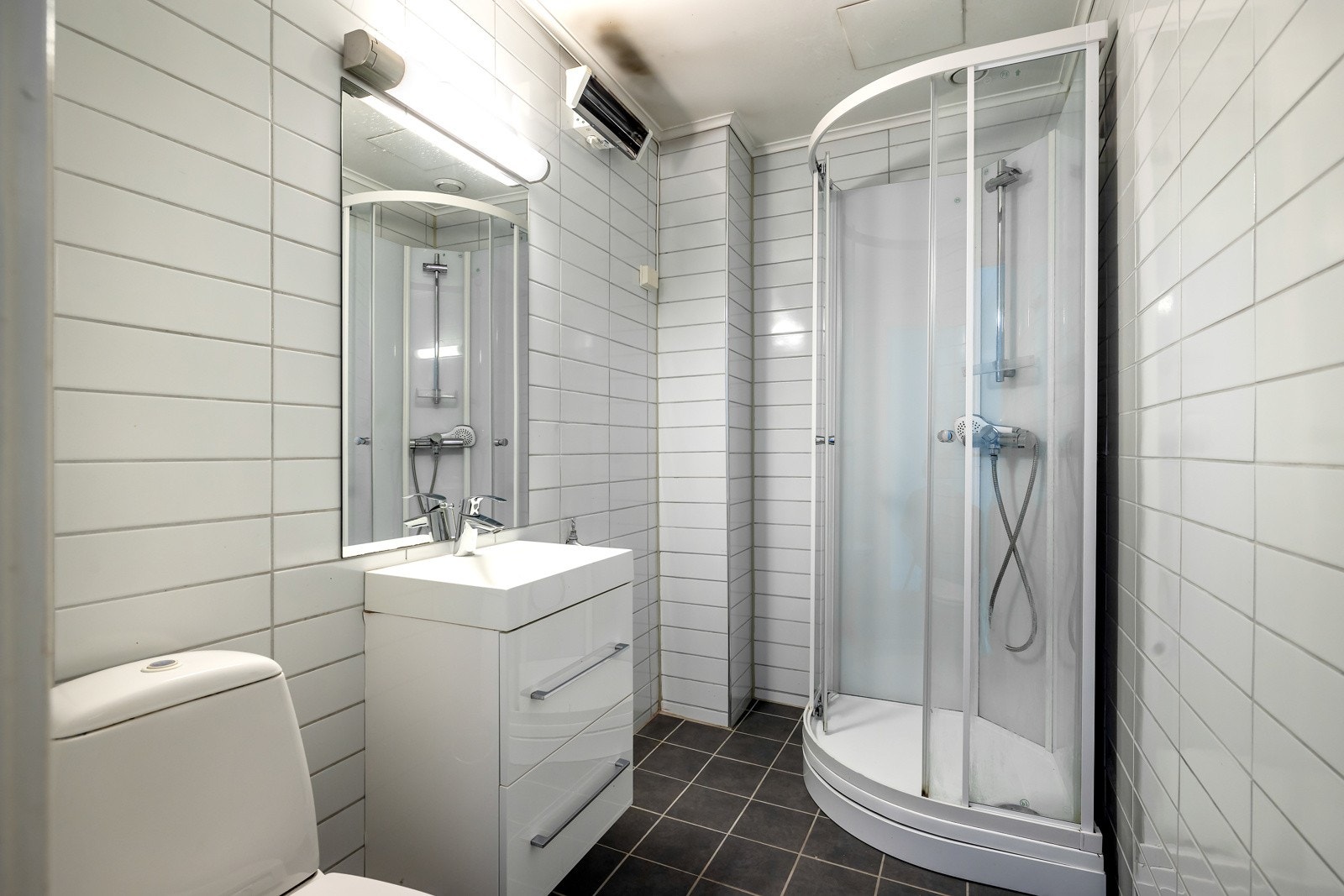 Leiligheten har et flislagt bad med behov for oppussing. Badet har dusjkabinett, toalett, servant med skapinnredning og opplegg for vaskemaskin Galleribilde