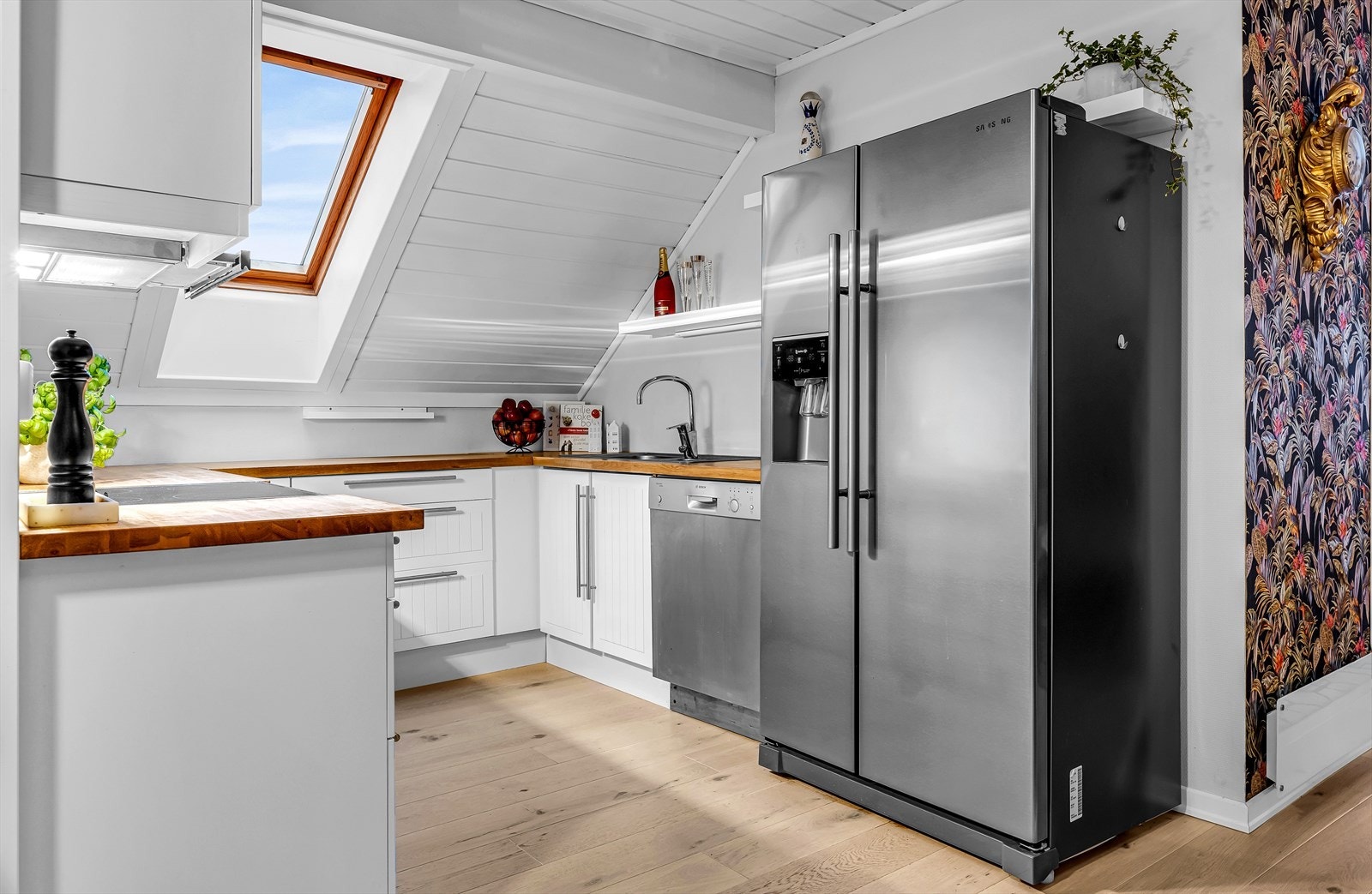 Kjøkkeninnredning med profilerte hvite fronter. Benkeplate av tre, nedfelt oppvaskkum i rustfritt stål med ett-greps armatur. Komfyr med keramisk platetopp. Oppvaskmaskin. Galleribilde