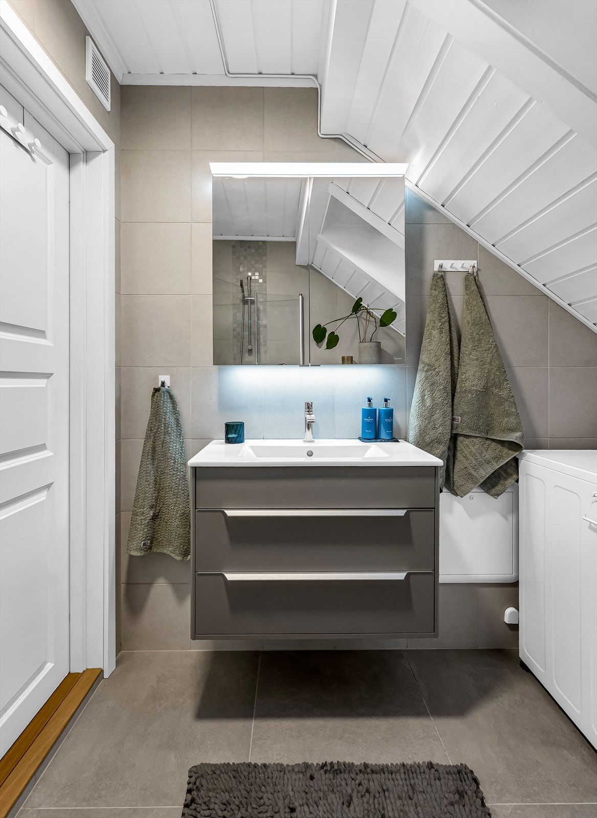 Ovenpåliggende servant med ett-greps armatur. Dusjsone med innfellbare dører i glass. Dusjarmatur tilkoblet hånddusj. Vegghengt toalett med innebygget sisterne og spalte for avrenning til sluk. Opplegg for vaskemaskin. Galleribilde