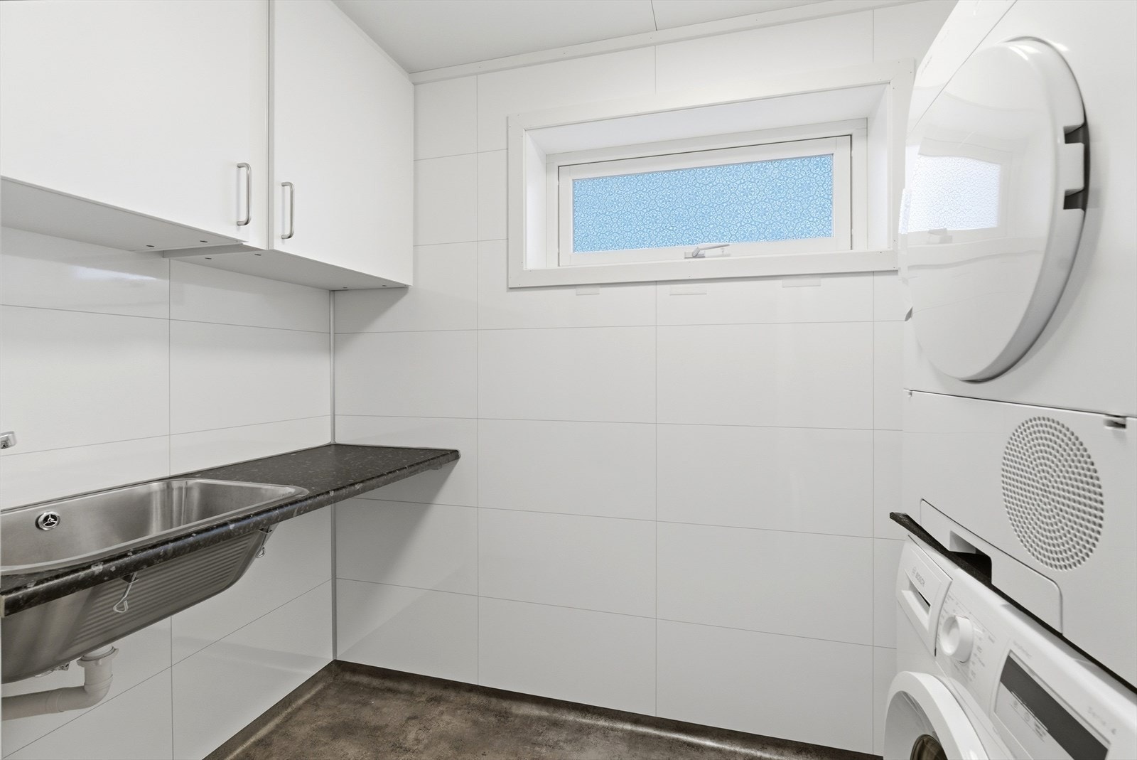 Vaskerom med opplegg for vaskemaskin og tørketrommel. Kjekk benk med vask og skap over. Galleribilde