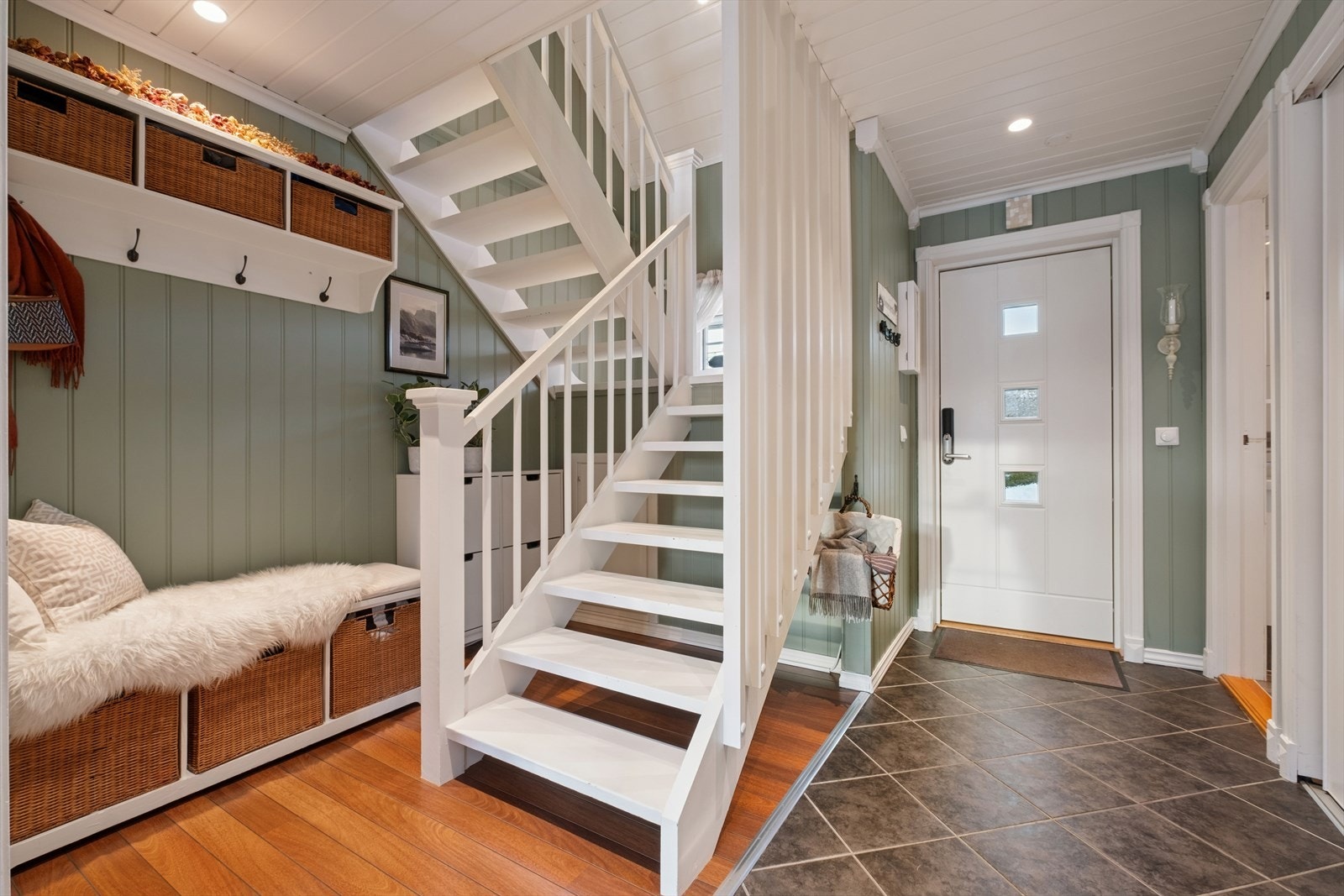 En lys og innbydende entré med flislagt gulv og hvitmalt trapp til andre etasje. Galleribilde