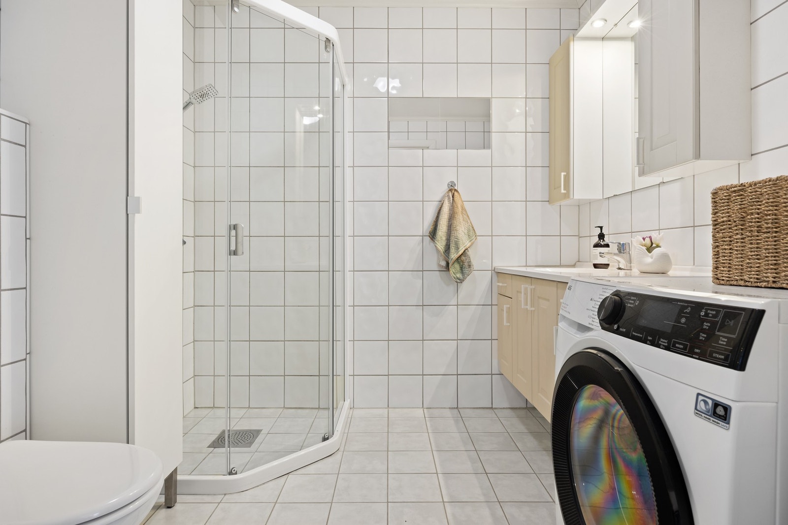 Flislagt baderom med varmekabler i gulv. Badet er utstyrt med toalett, dusjhjørne med skyvedør, servantskap, speil og overskap over servant. På badet er det også opplegg for vaskemaskin. Galleribilde