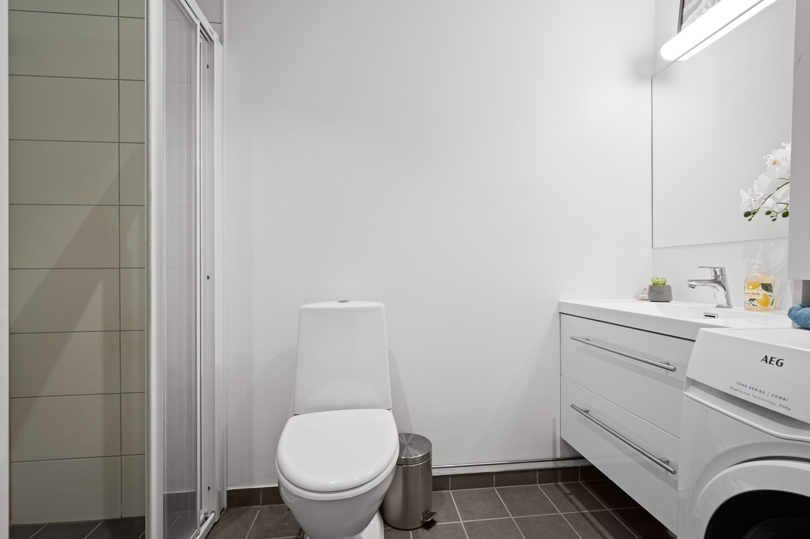 Bad med servant med underskap, toalett, dusjhjørne og opplegg til vaskemaskin. Galleribilde