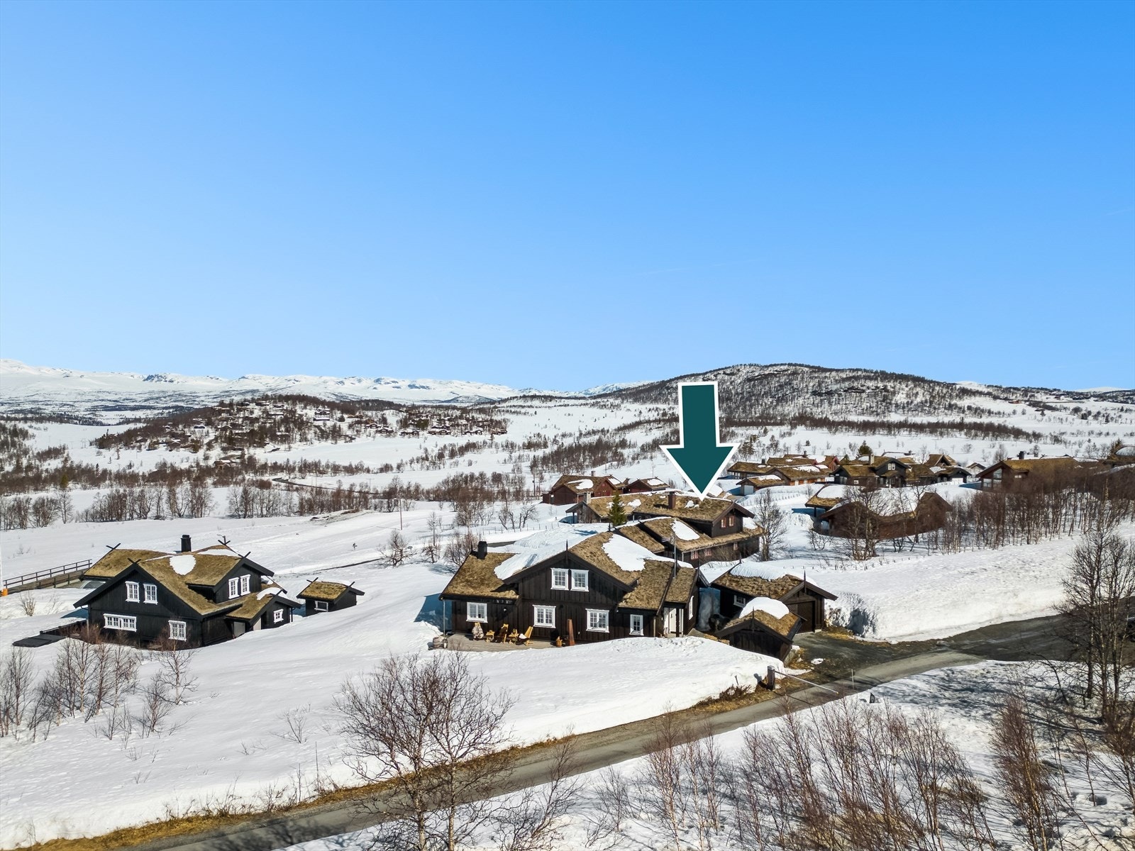 Elektrisk bom ved innkjøringen til hyttefeltet sikrer kontrollert adgang. Hytta ligger strategisk plassert for maksimal utsikt, markert med pil på bildet. Galleribilde