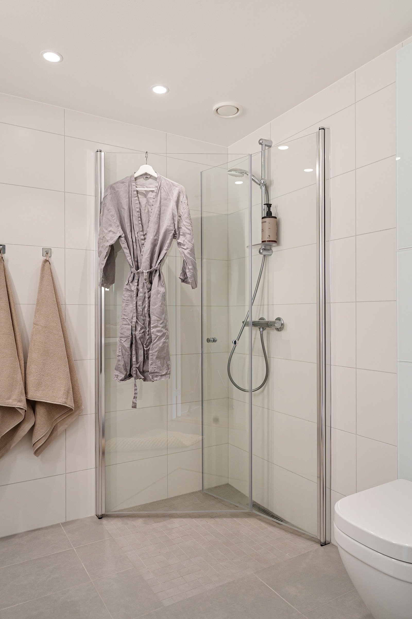 Badet oppleves svært praktisk og funksjonelt, og er videre utstyrt med veggmontert toalett, dusjhjørne med innfellbare glassdører, speil med integrert belysning og opplegg for vaskemaskin. Det er selvfølgelig behagelig varme i gulv. Galleribilde