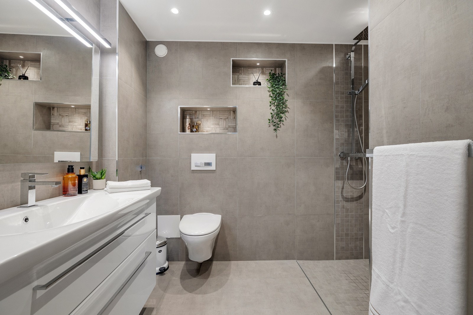 Lekkert flislagt baderom fra 2018 med varmekabler. Innredning med nedfelt servant, veggmontert toalett og dusjvegger/hjørne. Galleribilde