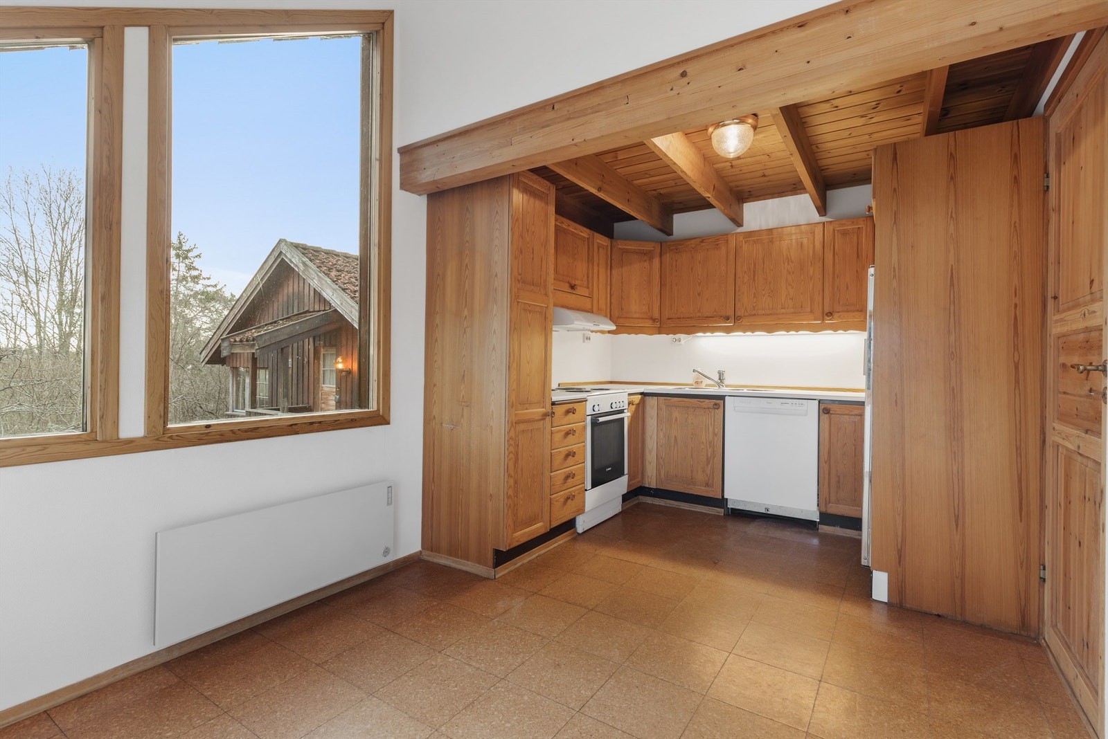 Kjøkken med flisbelegg. Vegger med malt strietapet. Skråtak med slett malt flate. Himling med panel og synlige bjelker. Kjøkkeninnredning fra byggeår. Benkeplater av laminat. Profilerte fronter. Malt strietapet mellom kjøkkenbenk og overskap. Galleribilde