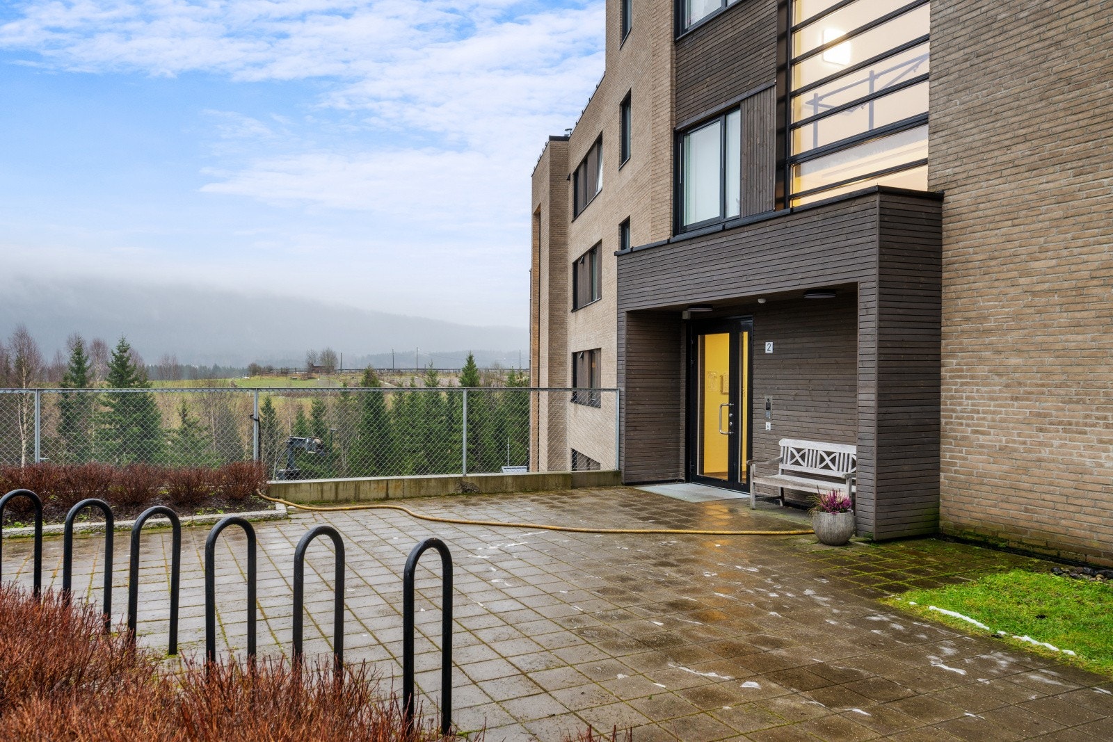 Inngangspartiet er moderne utformet. Sykkelparkering og hellebelagt plass. Galleribilde