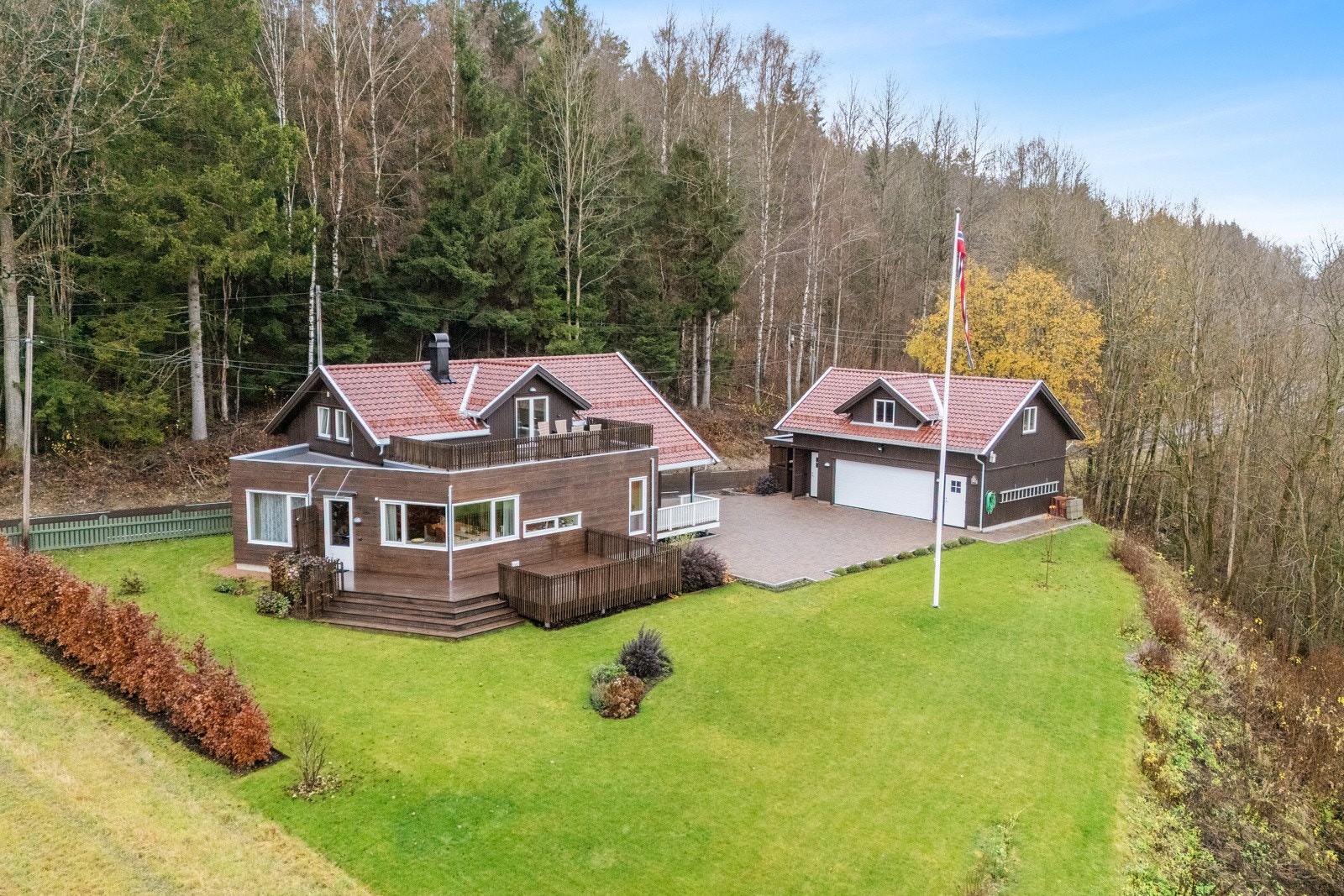 Sommerbildet viser en meget pent opparbeidet og beplantet eiertomt med plen og busker | steinsatt gårdsplass | Hollandsk Engobert takstein Galleribilde