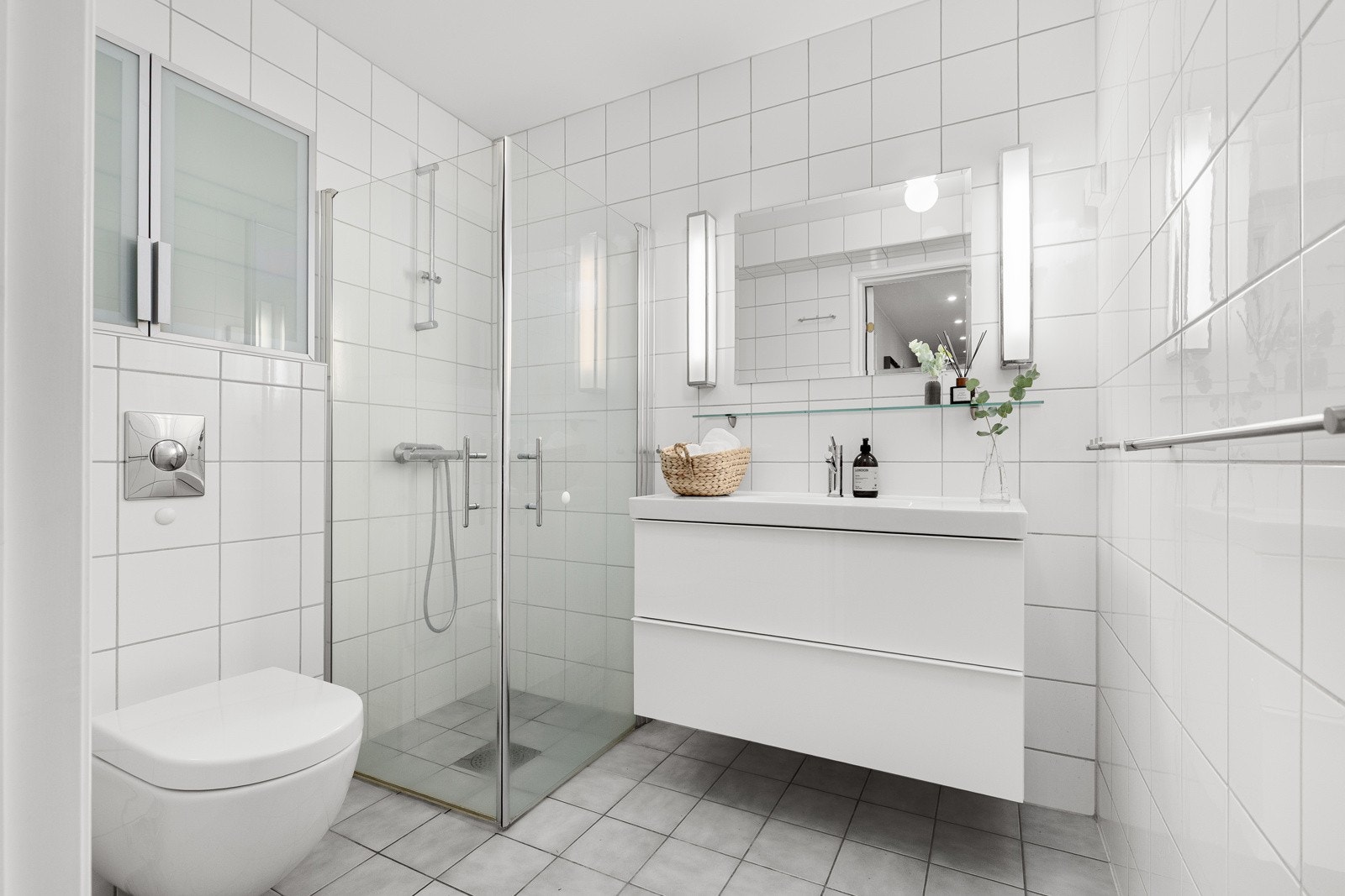 Badet, med adkomst fra hall, har innredning med slette fronter og heldekkende servant. Det er dusj med dører og vegghengt toalett Galleribilde