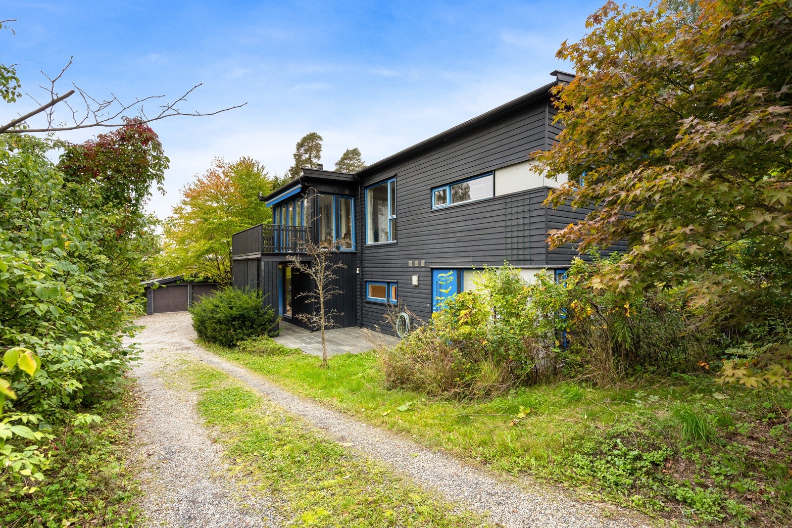 Skrånet tomt, pent opparbeidet med plen, prydbusker og flislagt uteplass. Gruslagt gårdsplass. Galleribilde
