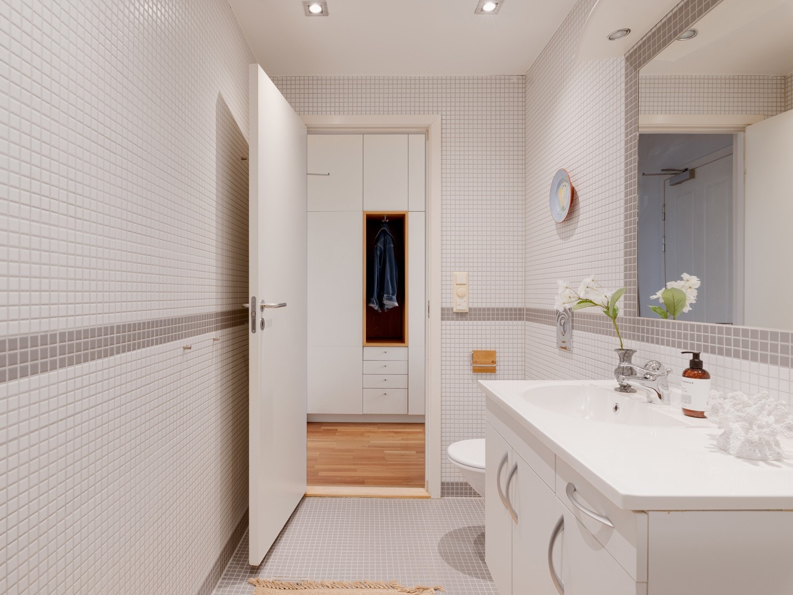 Badet er innredet med dusjnisje med glassvegger, veggmontert toalett, servant med innredning samt opplegg for vaskemaskin, og har mekanisk avtrekk tilknyttet sentral ventilasjon. Galleribilde